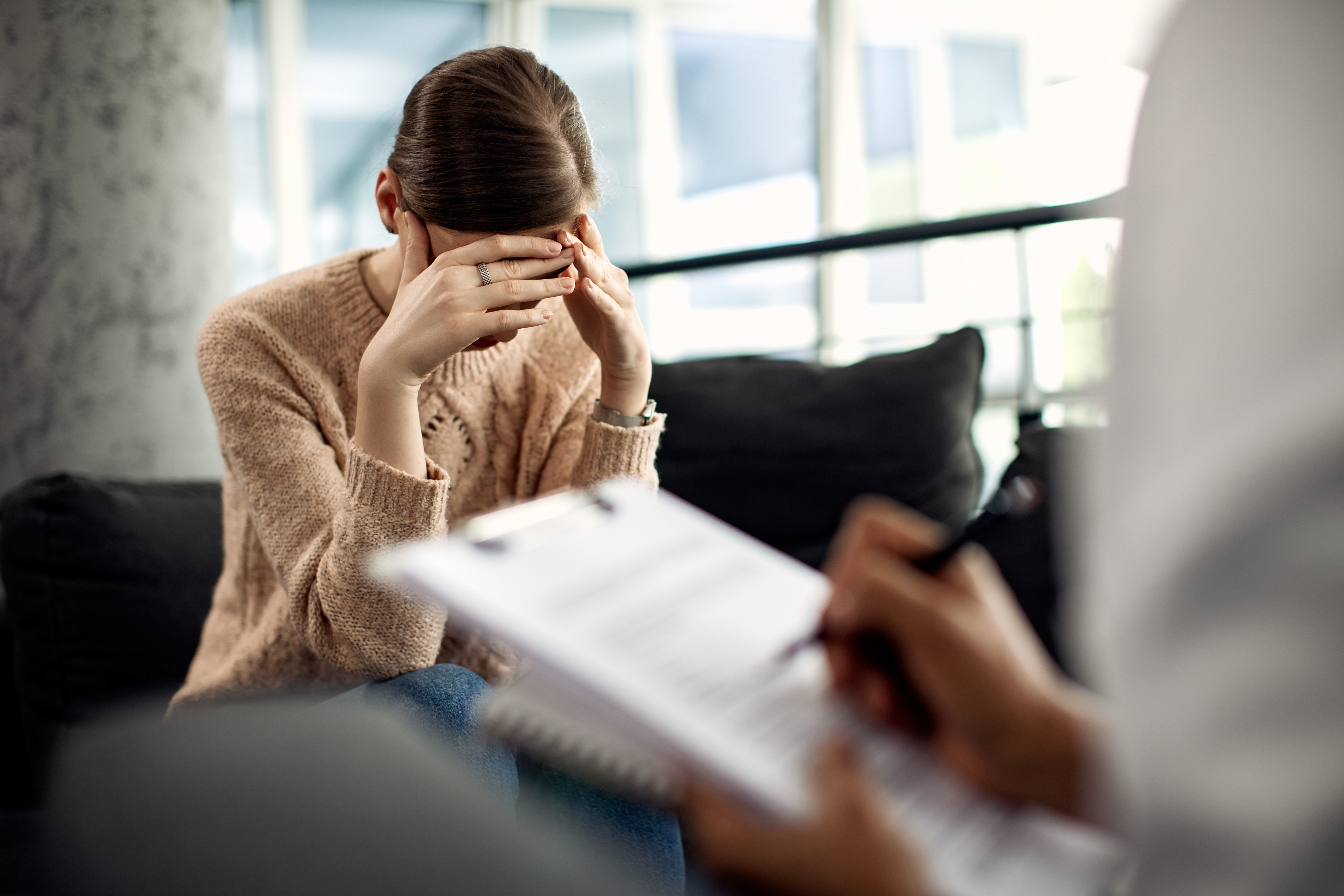 Depressed woman having psychotherapy session at doctor's office. Sad woman holding her head in pain while having a meeting with psychotherapist.